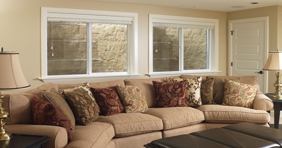 Finished basement family room with two large white-framed windows above a sectional sofa